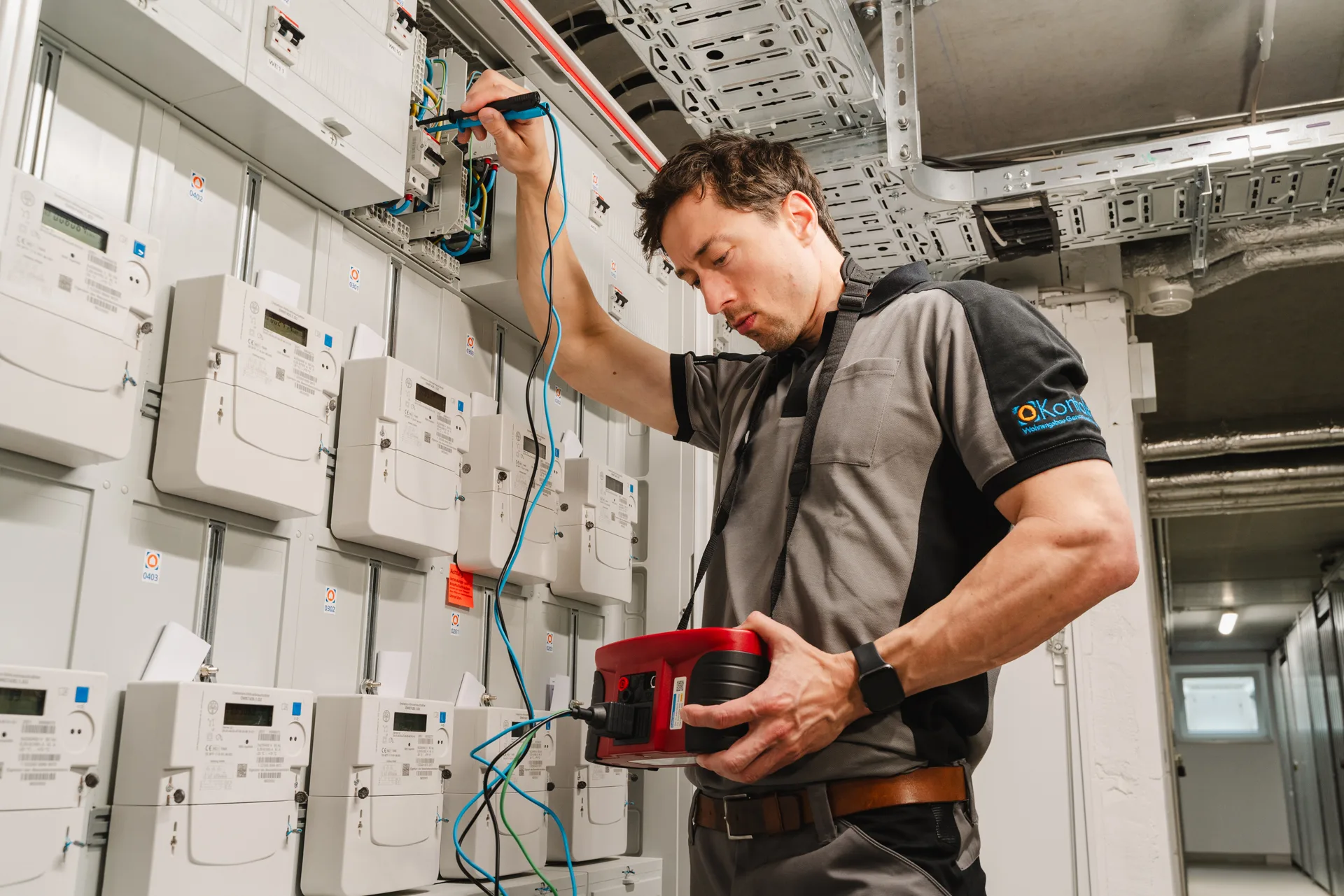 Elektriker prüft mit Messgerät die Verkabelung in einem Stromverteilerkasten in einem Technikraum.
