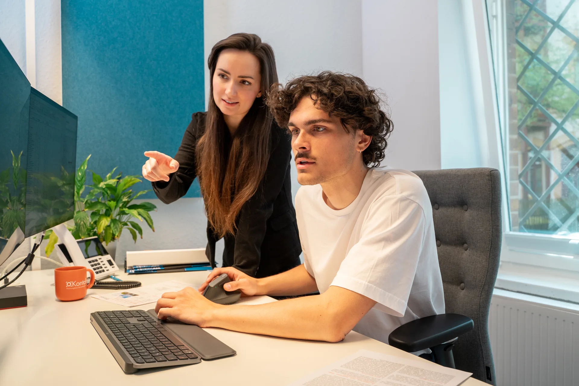 Zwei Mitarbeiter sitzen und stehen am Schreibtisch und schauen auf einen Computerbildschirm