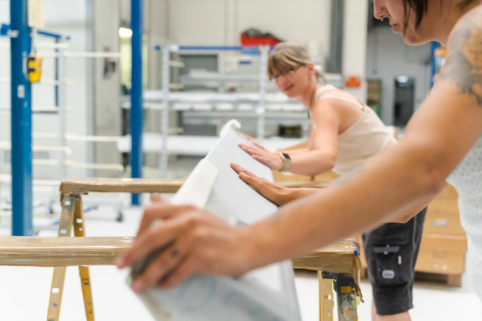 Zwei Frauen kontrollieren gemeinsam weiße Werkstücke in einer hellen Produktionshalle.