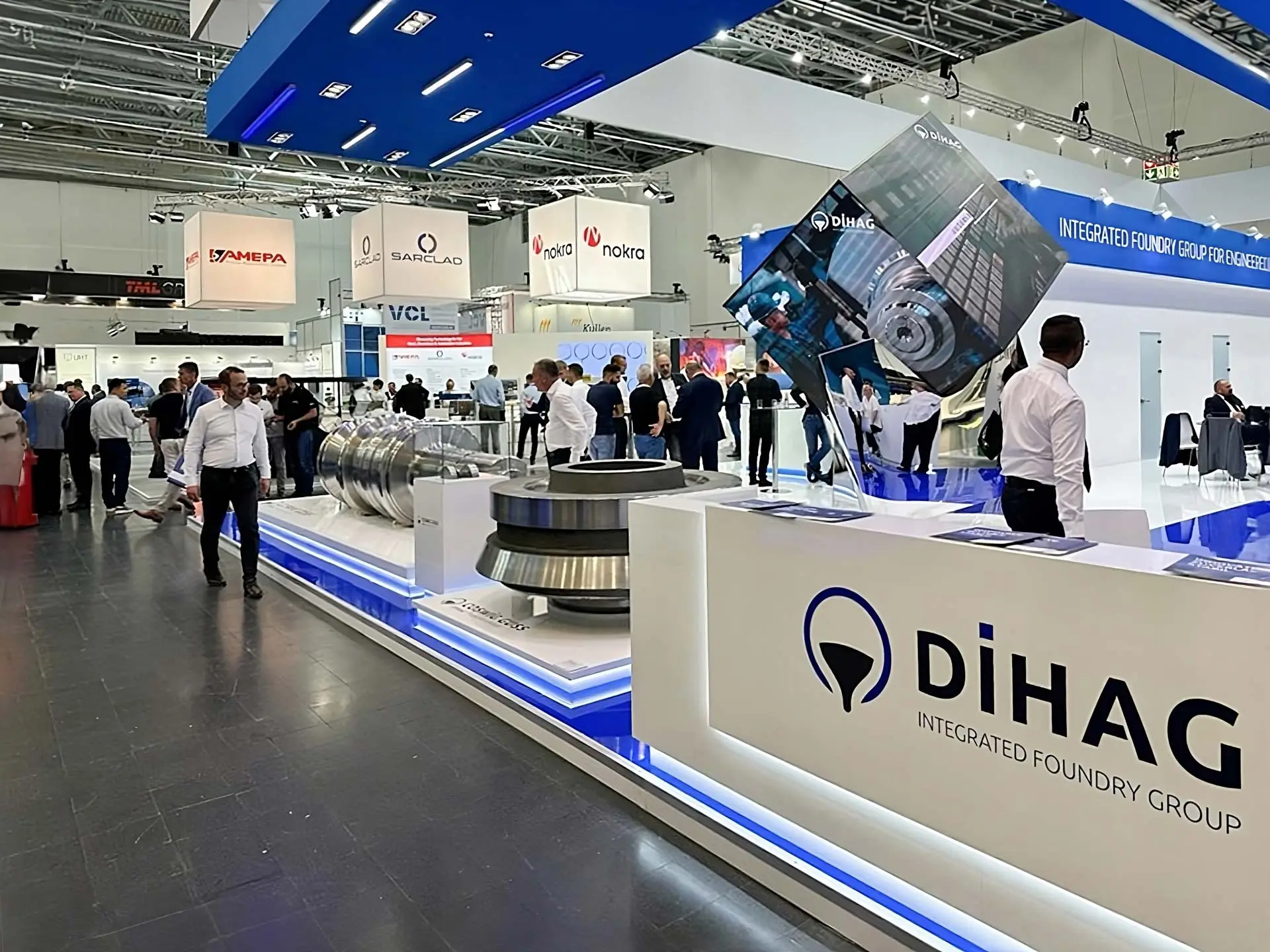 Blick auf den DIHAG-Messestand mit Exponaten aus Metall, Infotheke und Besuchergruppen auf der Messe.
